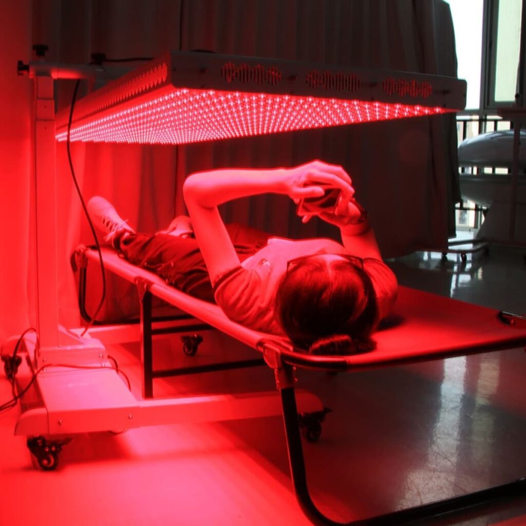 Red light therapy at home with person on bed under horizontal illuminated panel