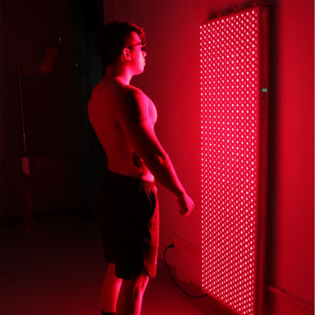 Person at home in front of red light therapy unit on wall
